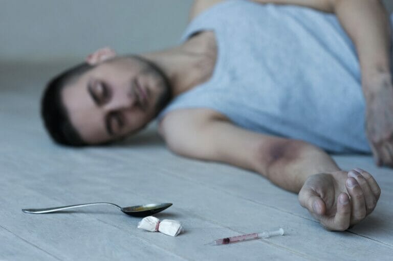 Heroin addict. Young man lying on the floor with syringe and pack of heroin laying near him